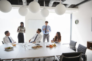 Businessmen And Businesswomen Meeting In Modern Boardroom Over Working Lunch