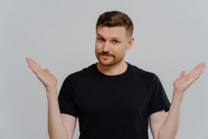 Isolated shot of confused young guy spreading hands sideways and feeling doubt while making choice