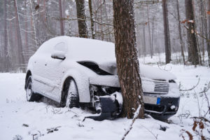 Broken car crashes into tree after losing control on slippery road in snowy forest.