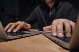 partial view of hacker using laptops at tabletop with smartphone, cyber security concept