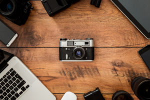 Displacement of old technology. Top view of retro camera surrounding by diverse equipment for photographer laying on the wooden grain