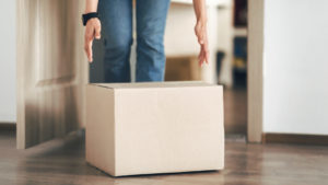 Unrecognizable person picking cardboard box up from the floor