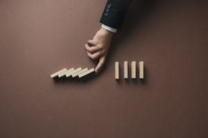 Hand of a businessman intervening a collapsing dominos to stop t