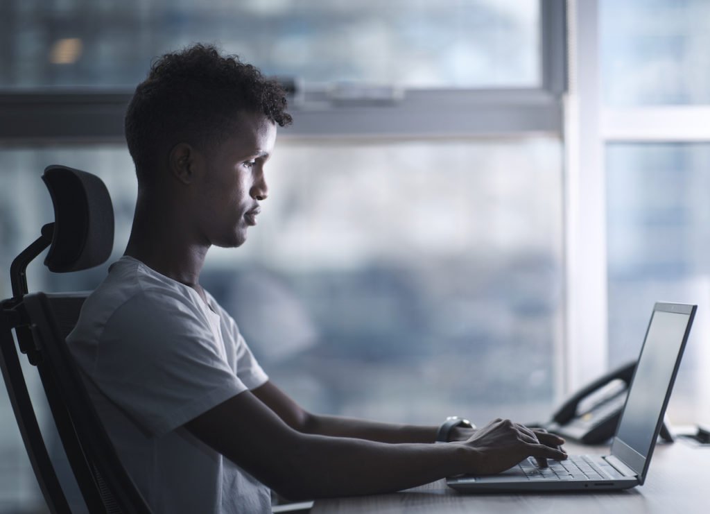 Young handsome black man concentrated focused to his laptop and working in serious mood in a modern office. copy space include profile shot.