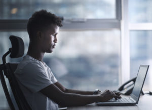 Young handsome black man concentrated focused to his laptop and working in serious mood in a modern office. copy space include profile shot.